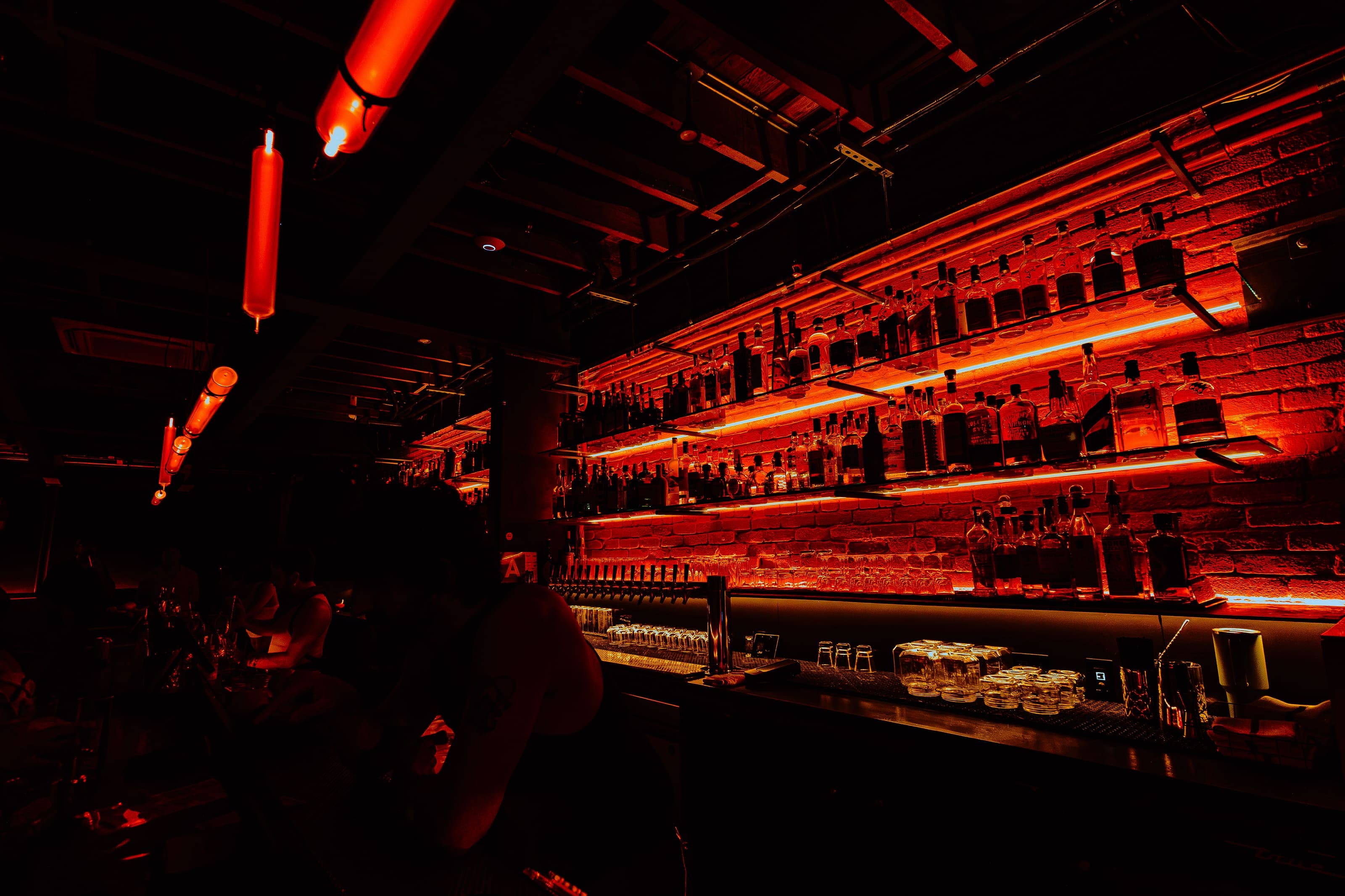 The glowing red-lit back bar at Animal LA, shelves of bottles under neon strips, with a patron silhouetted in the foreground