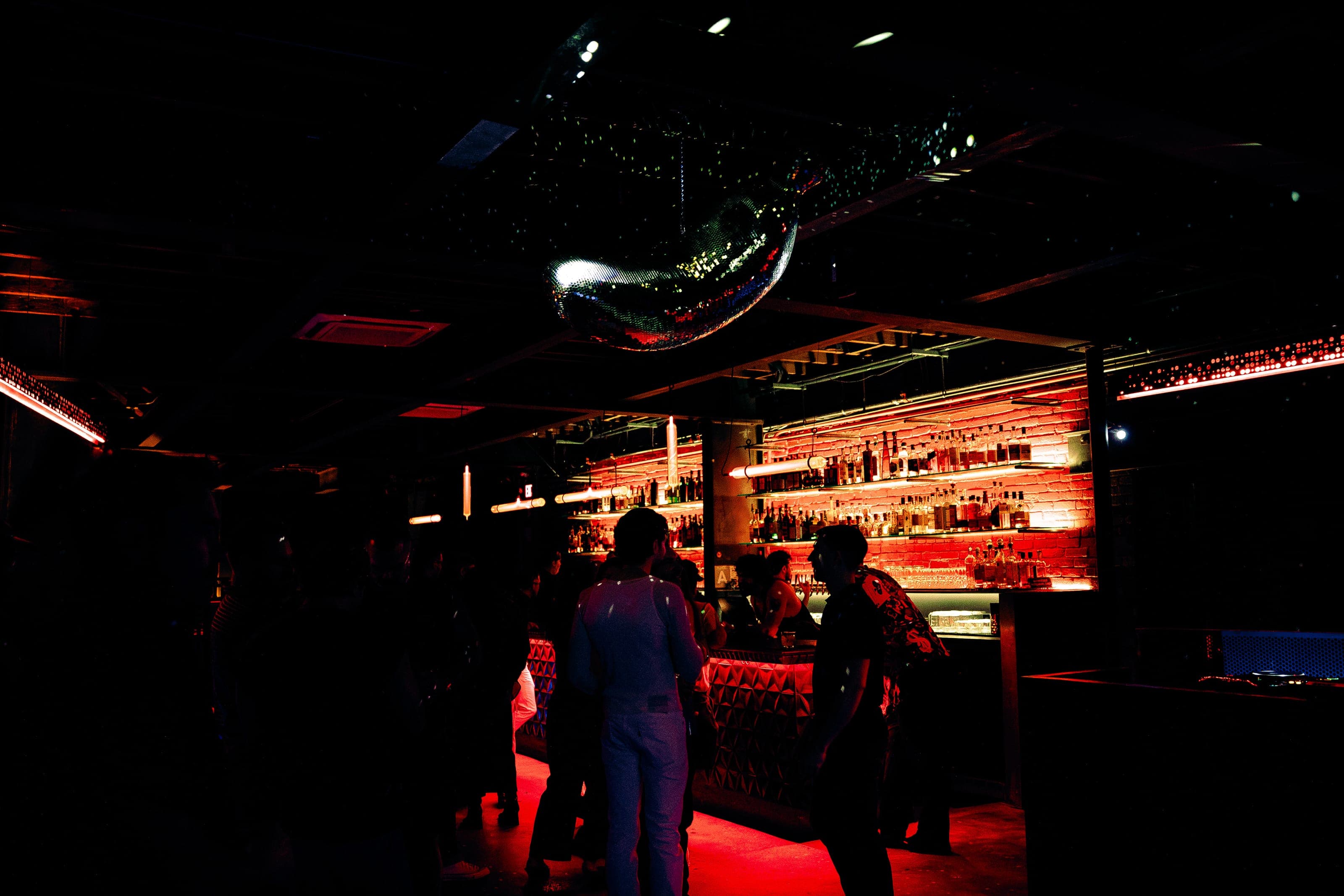 A mirrored disco ball above the dim main room, with guests gathered at the bar under red light