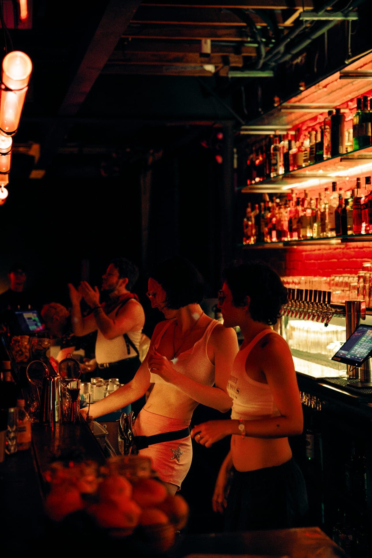Bartenders at work behind the lit back bar, with a red neon strip glowing on the left