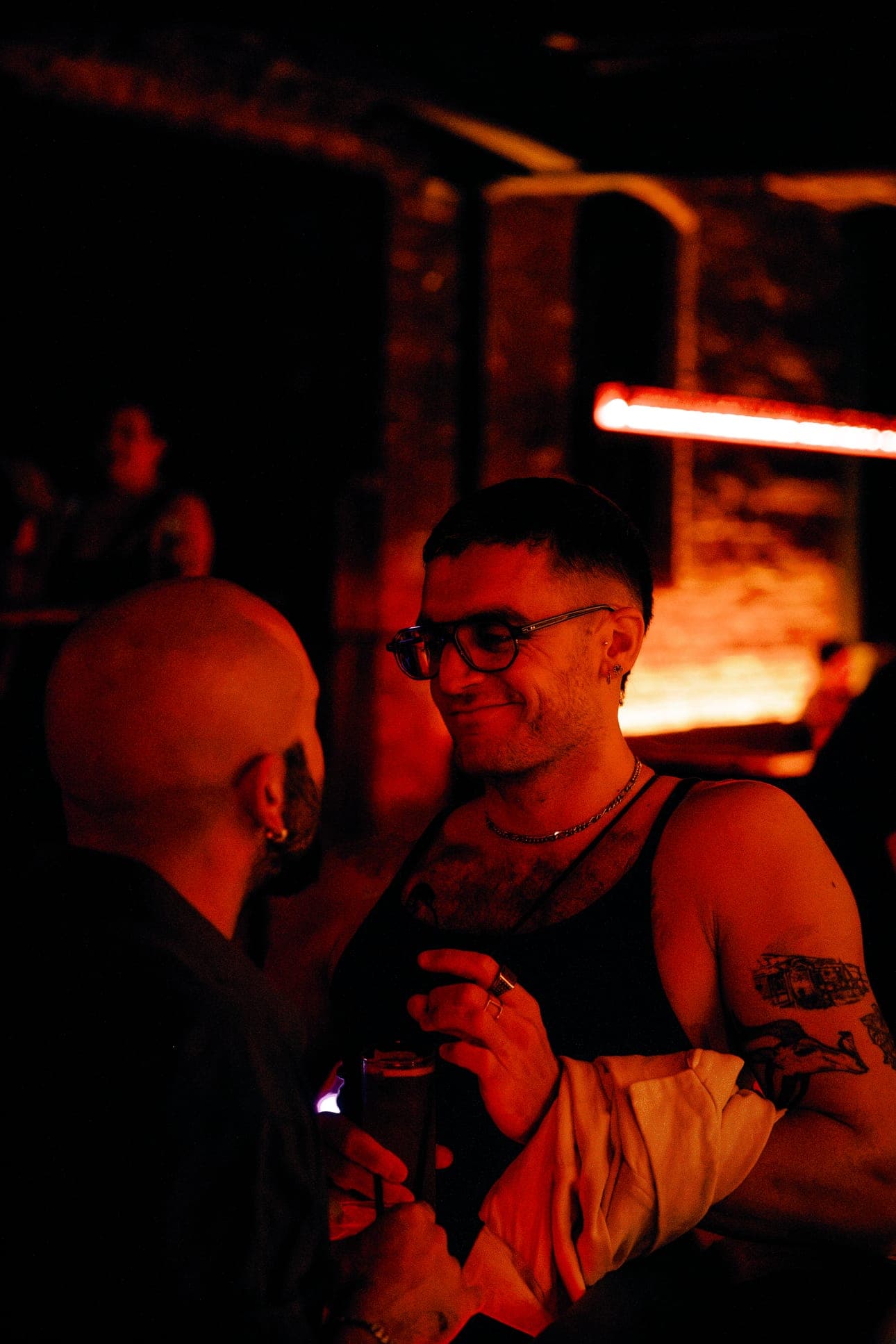 A smiling patron in glasses holding a drink, in warm red light
