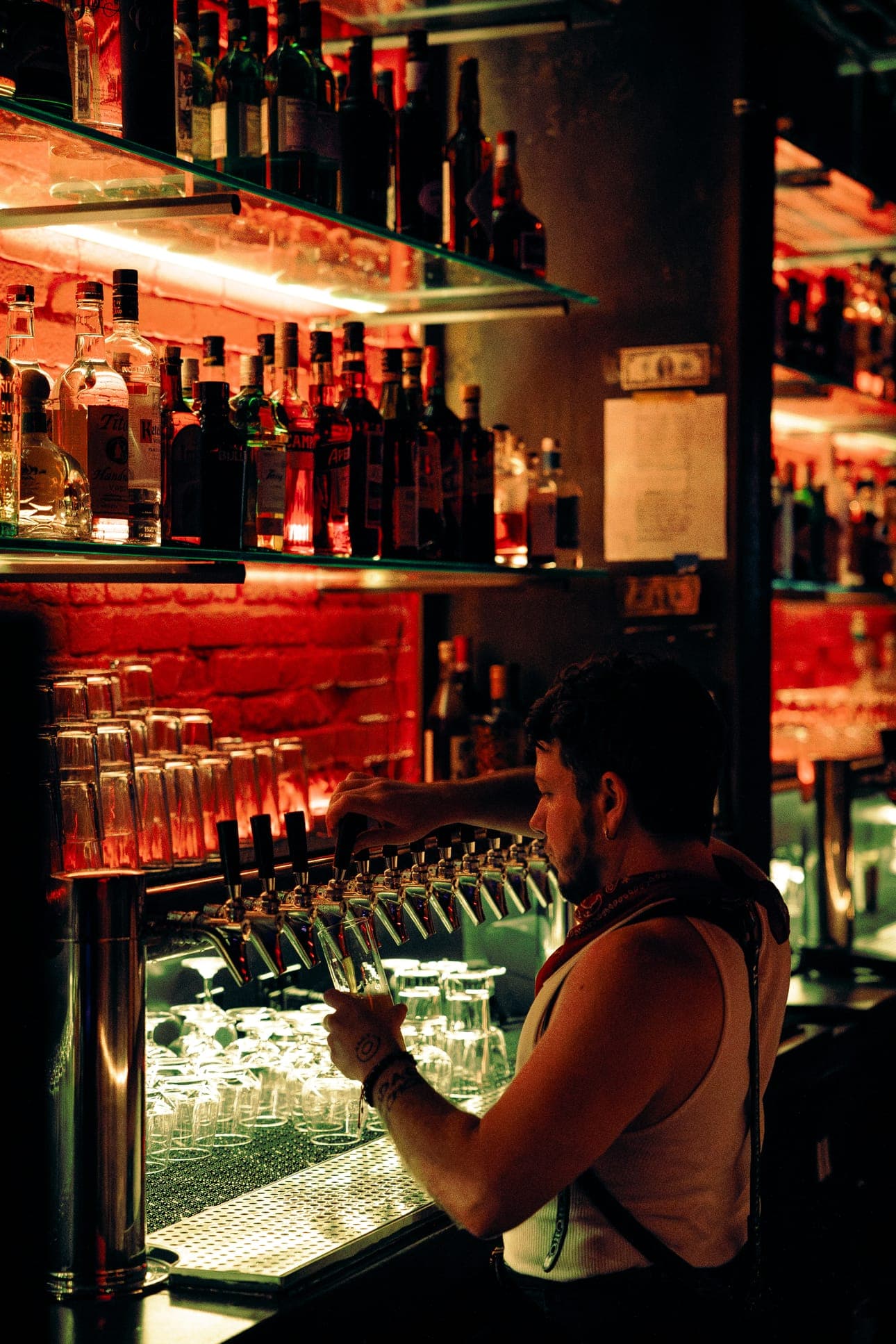 A bartender in a tank top and apron pulling a beer from the taps